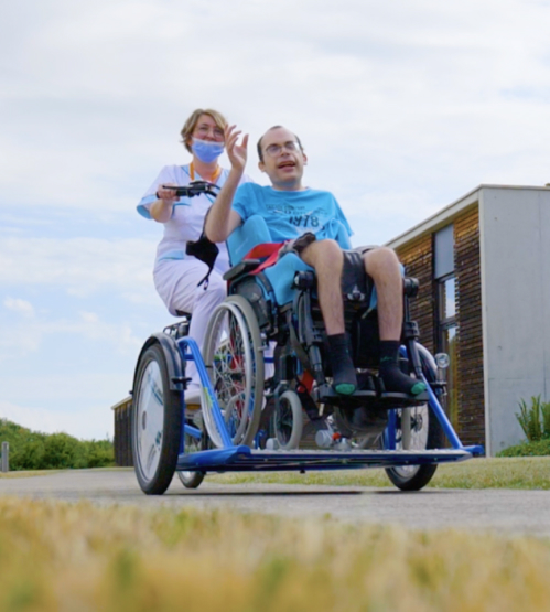 personne en situation de handicap sur un vélo plateforme avec une aide soignante